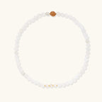 Three layered white beaded bracelets with carved orange agate lotus centerpiece and freshwater pearls on cream background.