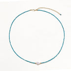 Delicate gold vermeil necklace with teal apatite beads and freshwater pearl on white background.
