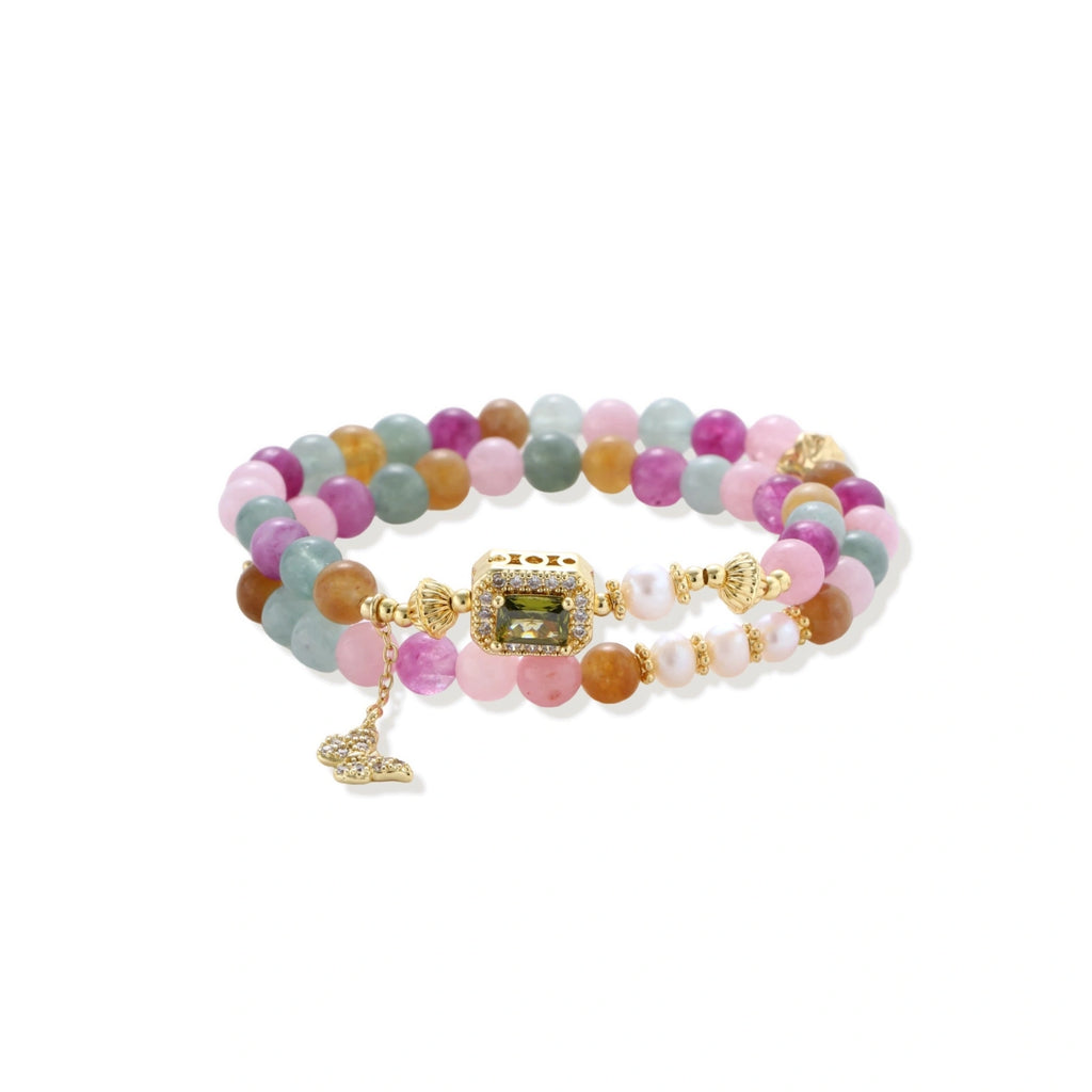 Stretchable bracelet with pastel gemstone beads, freshwater pearls, gold centerpiece and butterfly charm on cream background