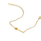 Delicate gold chain bracelet with minimalist bar and centered knot detail on cream background