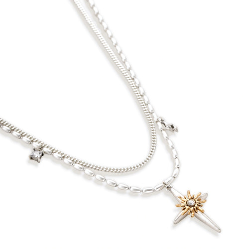 Layered silver-toned necklace set with cross pendant and gold sun charm detail, matching drop earrings on white background.