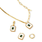 Gold-plated jewelry set with white enamel square pendants and emerald CZ stones on cream background.