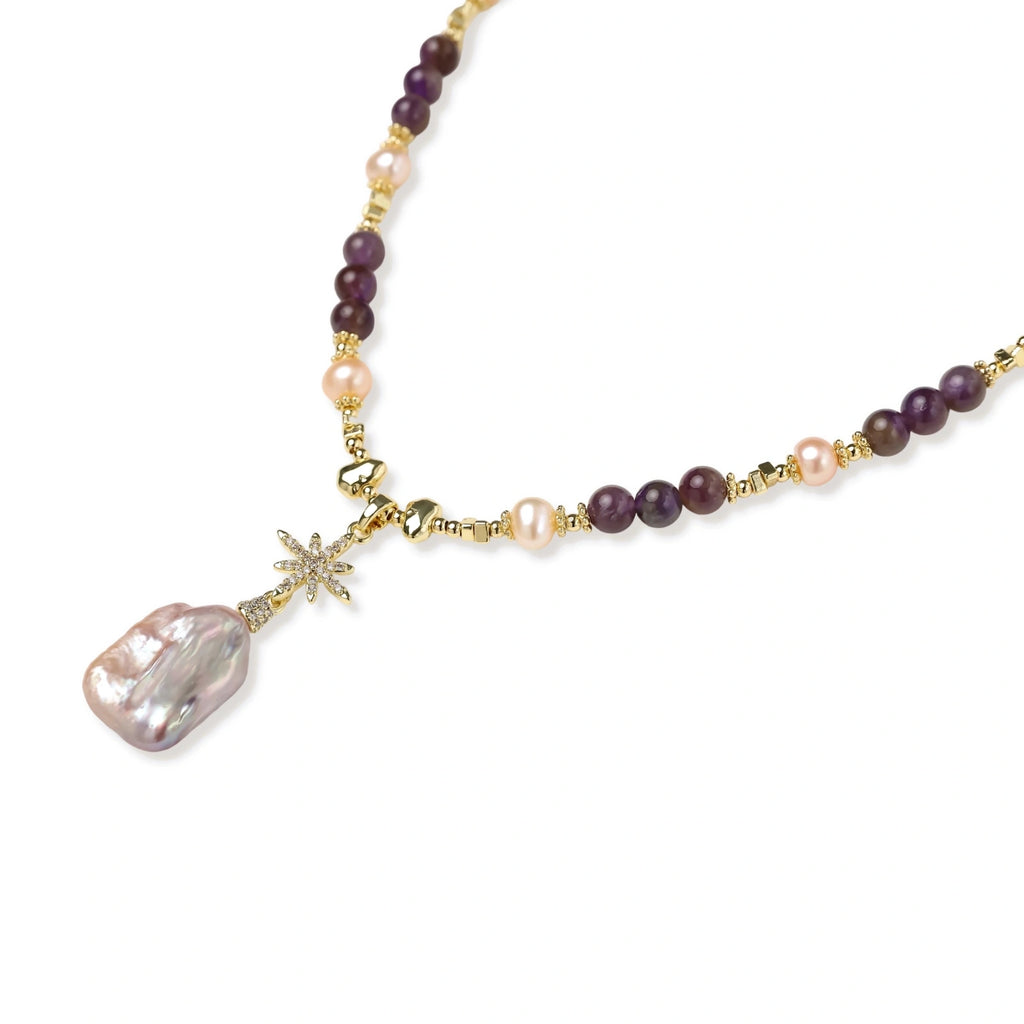 Gold necklace with iridescent baroque pearl pendant, purple amethyst beads, and crystal star charm on cream background