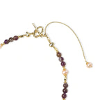 Gold necklace with iridescent baroque pearl pendant, purple amethyst beads, and crystal star charm on cream background